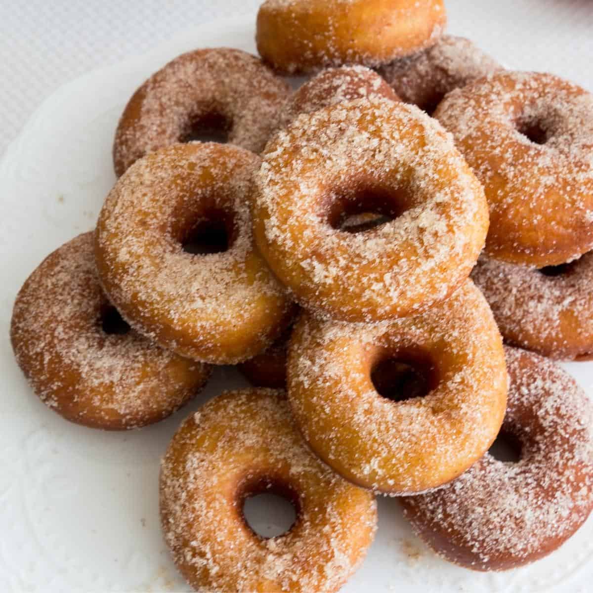 A stack of sugar donuts on a cake stand.