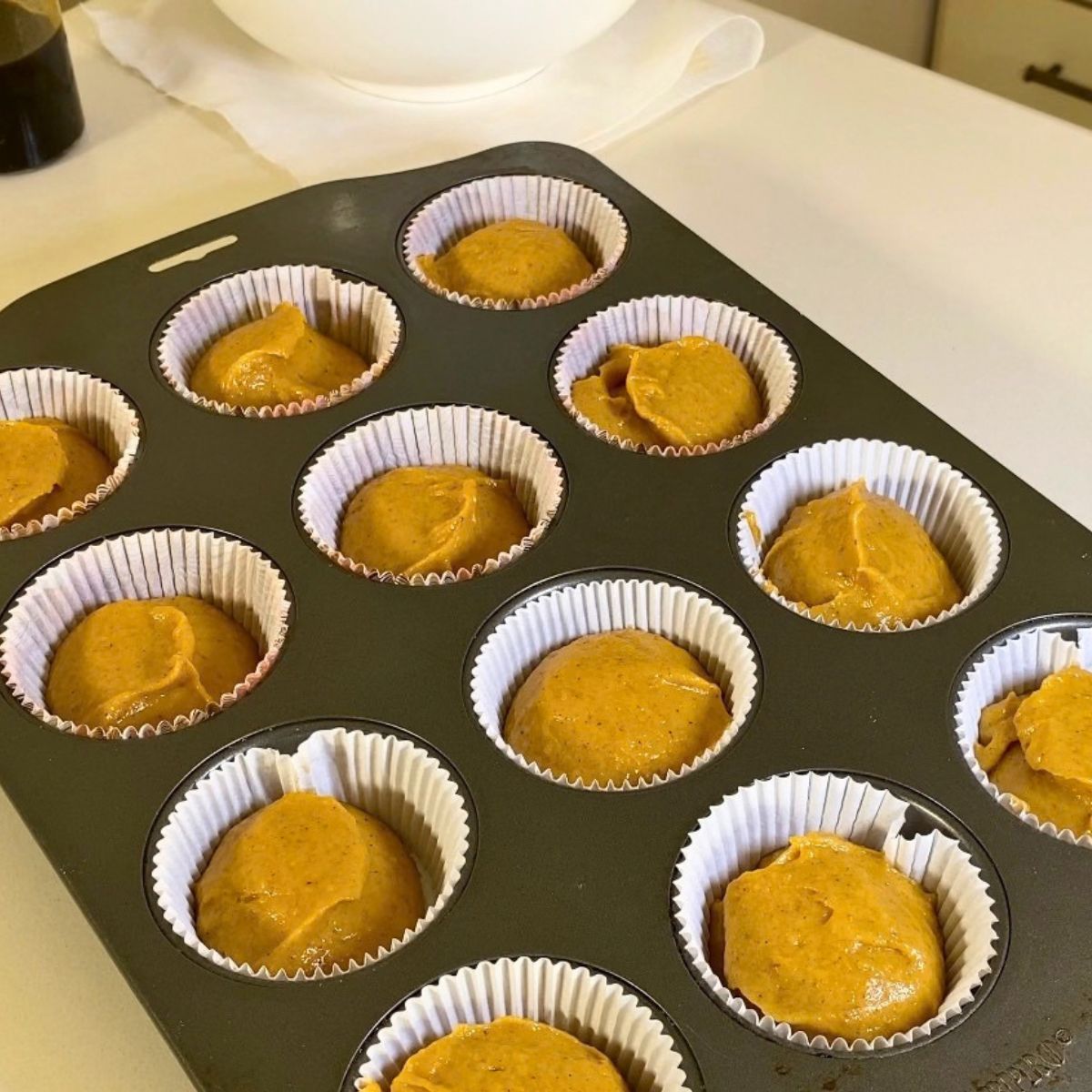 A cupcake pan with pumpkin cupcakes batter.