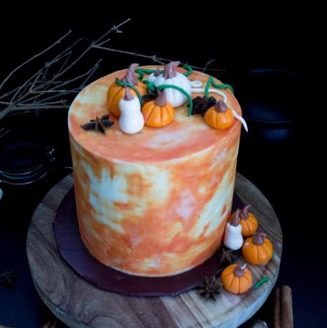 A frosted cake with fondant pumpkins on top