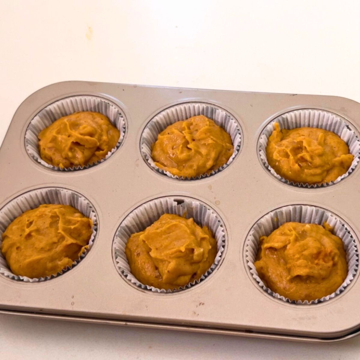 Muffin pan with pumpkin muffins ready for baking.