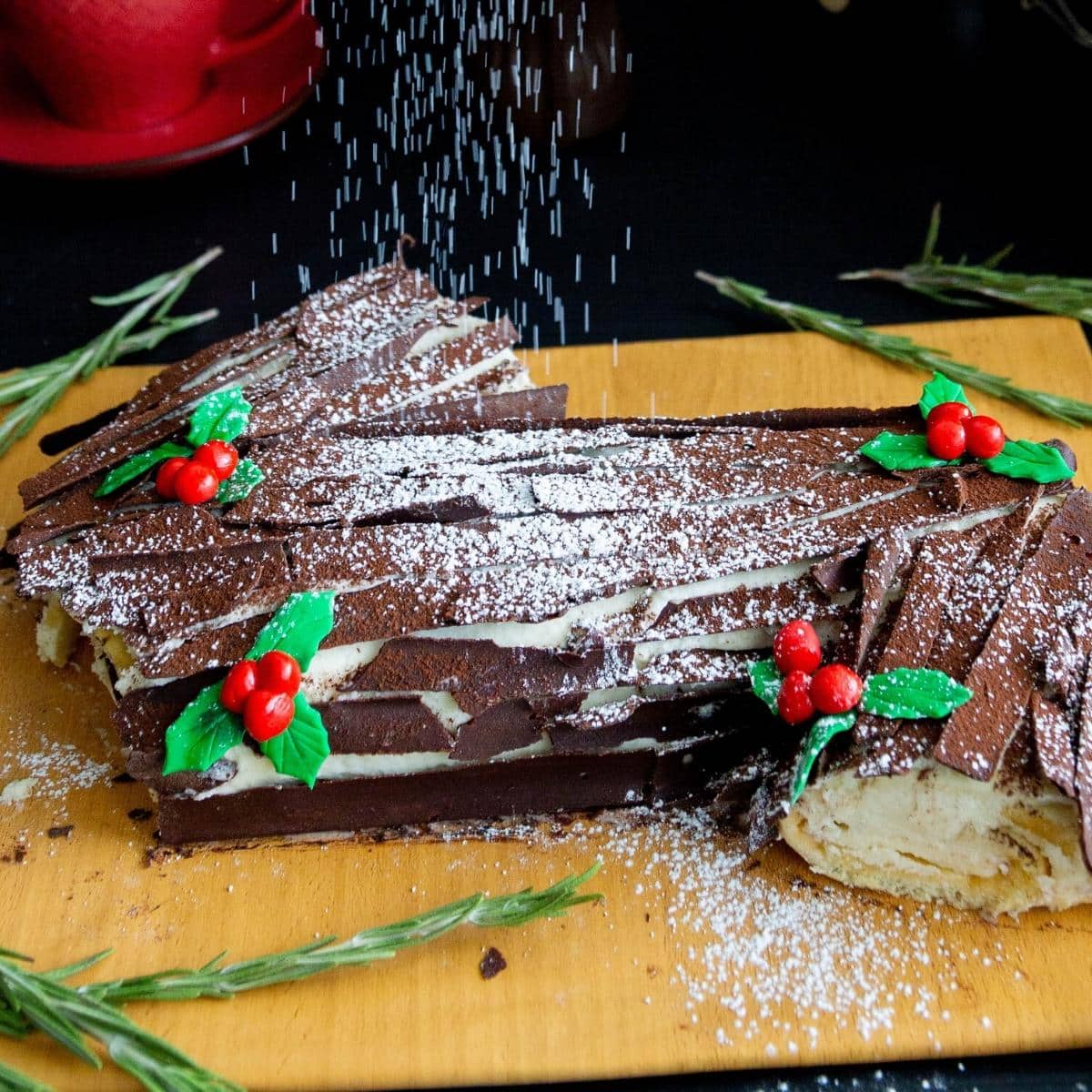 Christmas log cake on a wooden board with berries and rosemary.