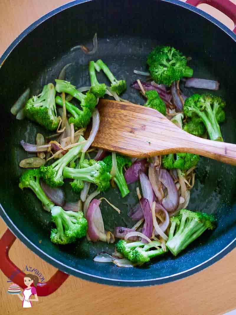 A skillet with broccoli and red onions.