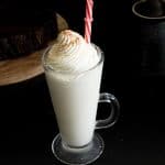 A tall glass of eggnog with whipped cream on top.