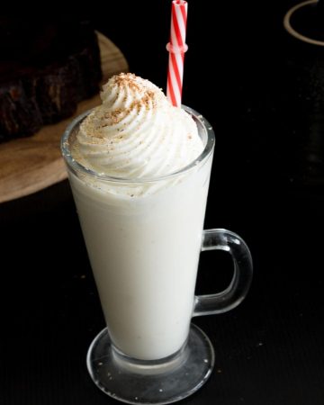 A tall glass of eggnog with whipped cream on top.