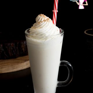 A tall glass of eggnog with whipped cream on top.