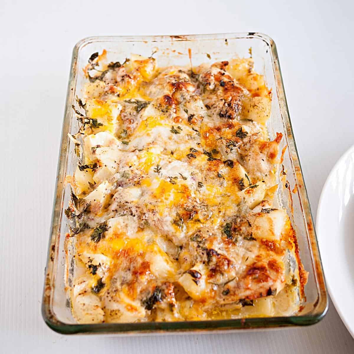 A glass casserole dish with baked chicken and potatoes.