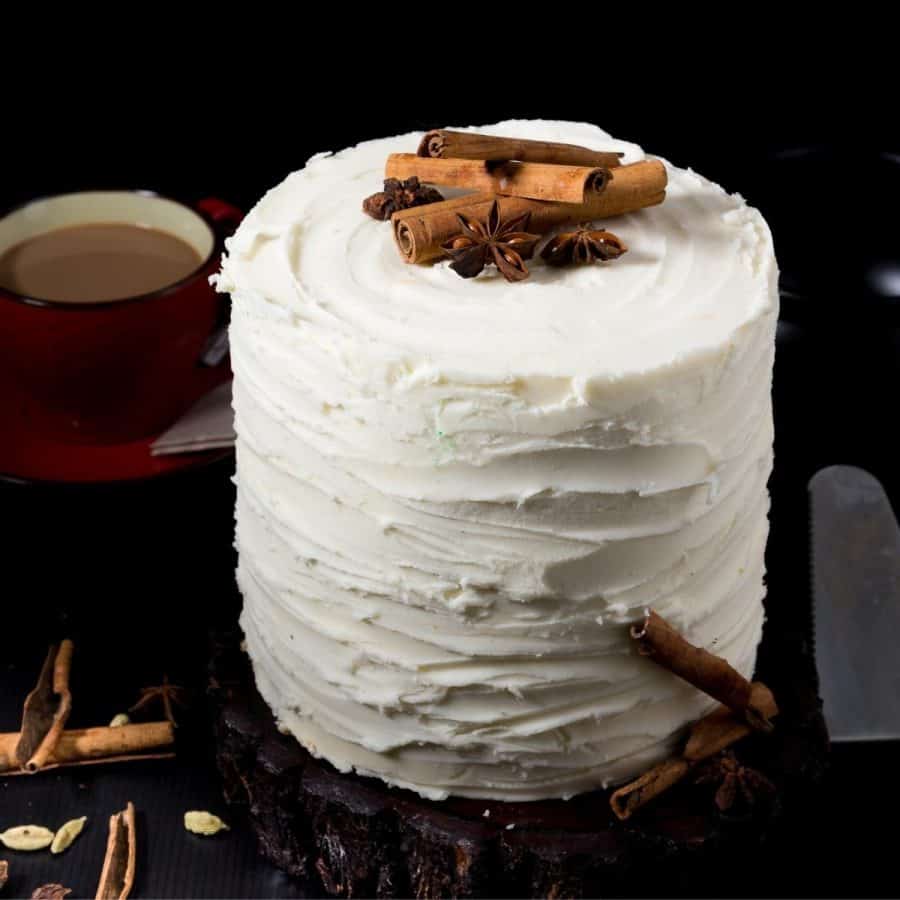 A layer cake with buttercream frosting and whole chai spices on top.