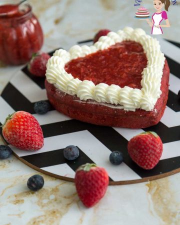 A red heart-shaped cake on a round board.