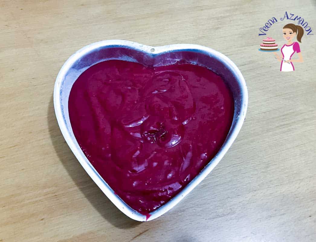 Red cake batter in a heart-shaped baking pan.