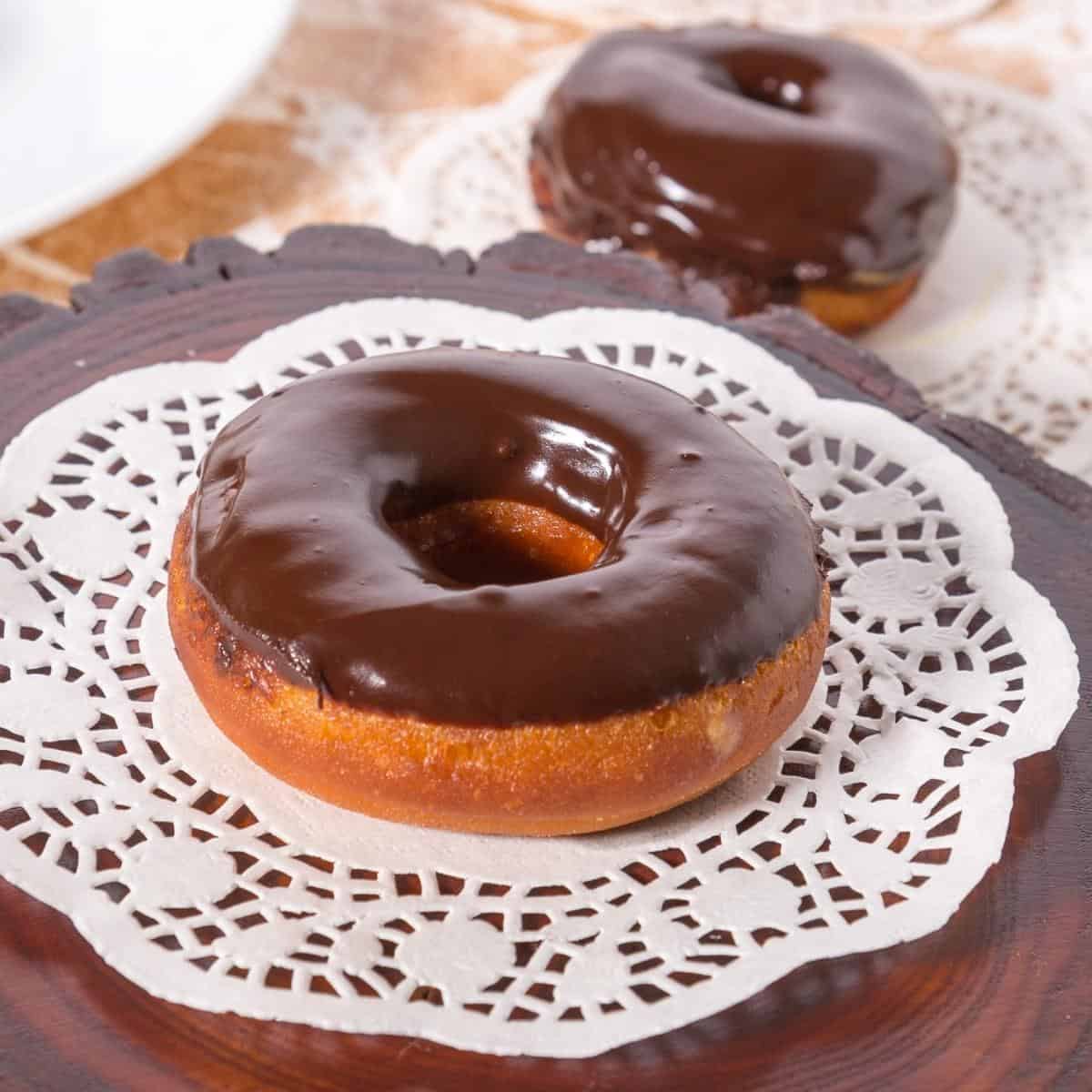 A glazed chocolate donut on a a white doily