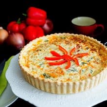 Quiche with red peppers on a cake stand.