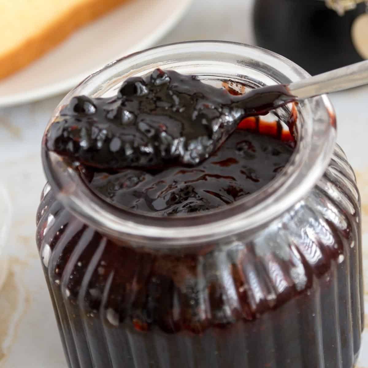 A spoon full of blueberry jam over a mason jar.