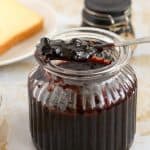 A jar of blueberry jam with a spoon full of jam.