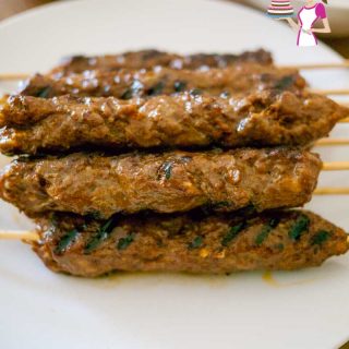 A stack of kebabs made with beef on a tray served with tahini, pita and hummus.
