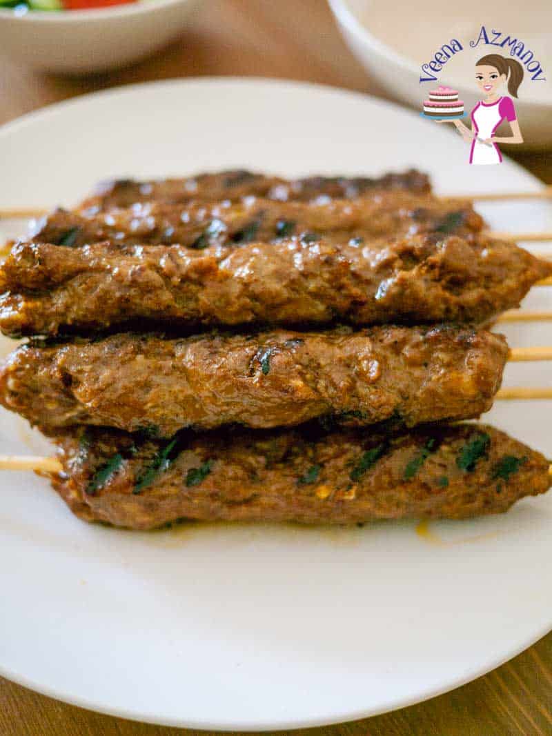 A stack of kebabs made with beef on a tray served with tahini, pita and hummus.