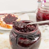 Mixed berries jam in a jar with a spoon.