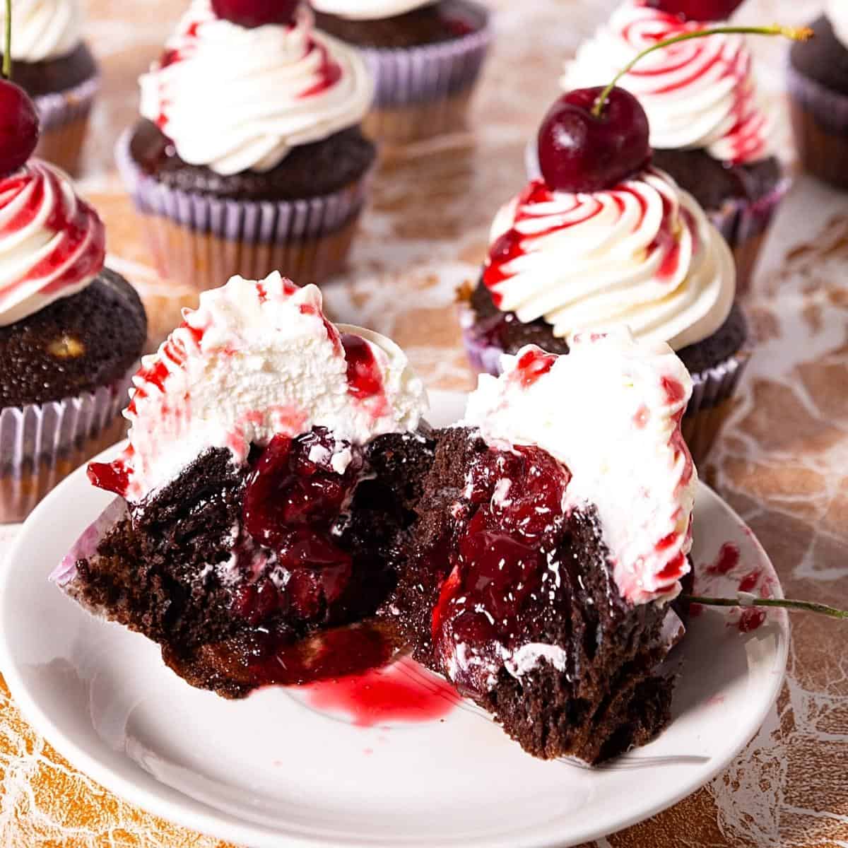 A cut chocolate cupcake with cherry filling and frosting.