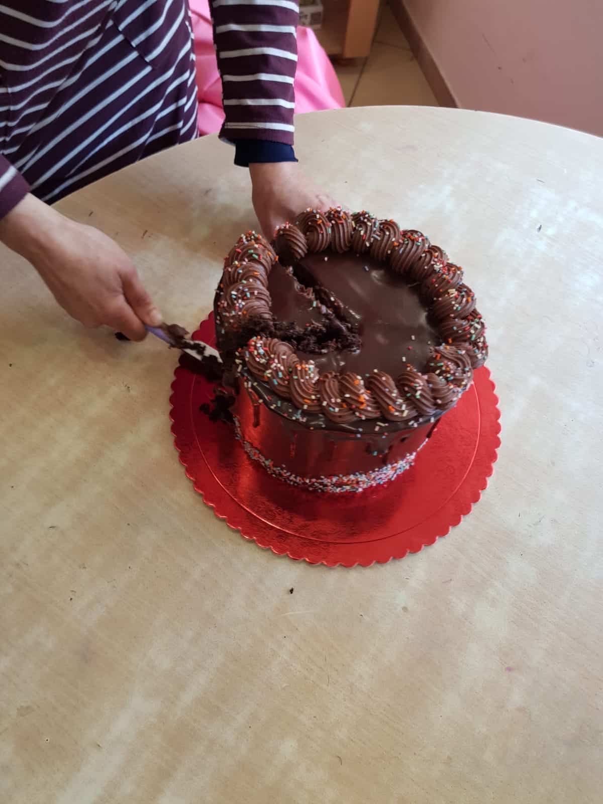 A person cutting a piece of chocolate cake on a table.