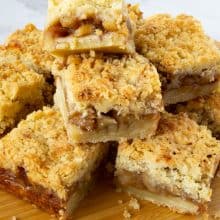 Apple pie bars stacked on a wooden board.