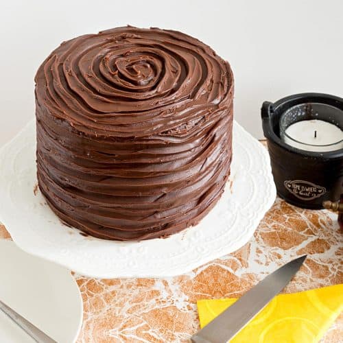 A frosted chocolate cake on the cake stand.