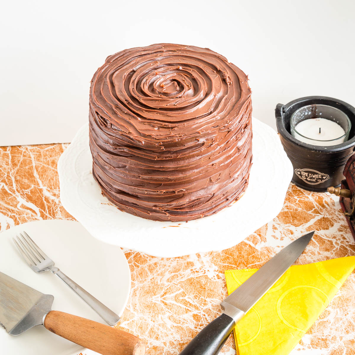 A frosted chocolate cake on the cake stand.