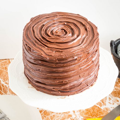 A frosted chocolate cake on the cake stand.