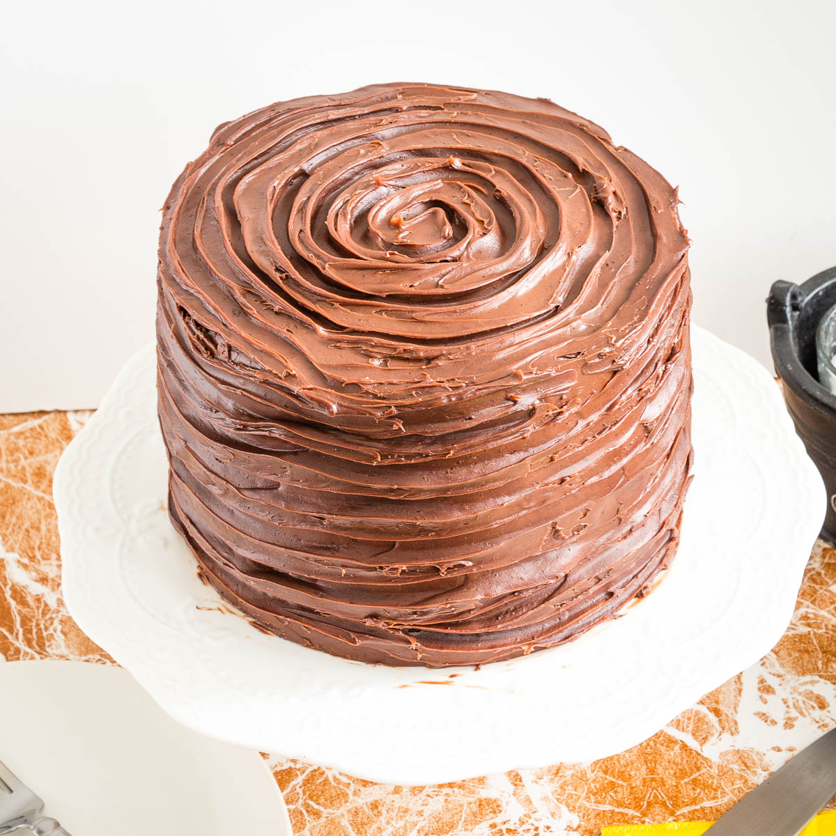 A frosted chocolate cake on the cake stand.
