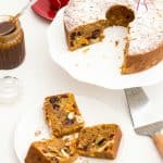 Slices of fruit cake on a plate next to the remaining cake on a cake stand.