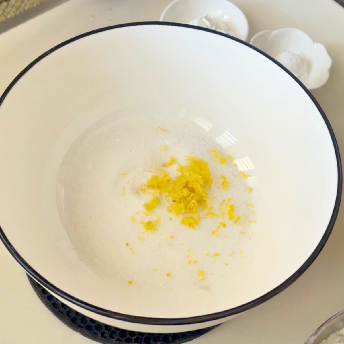 A white bowl with sugar and lemon zest.