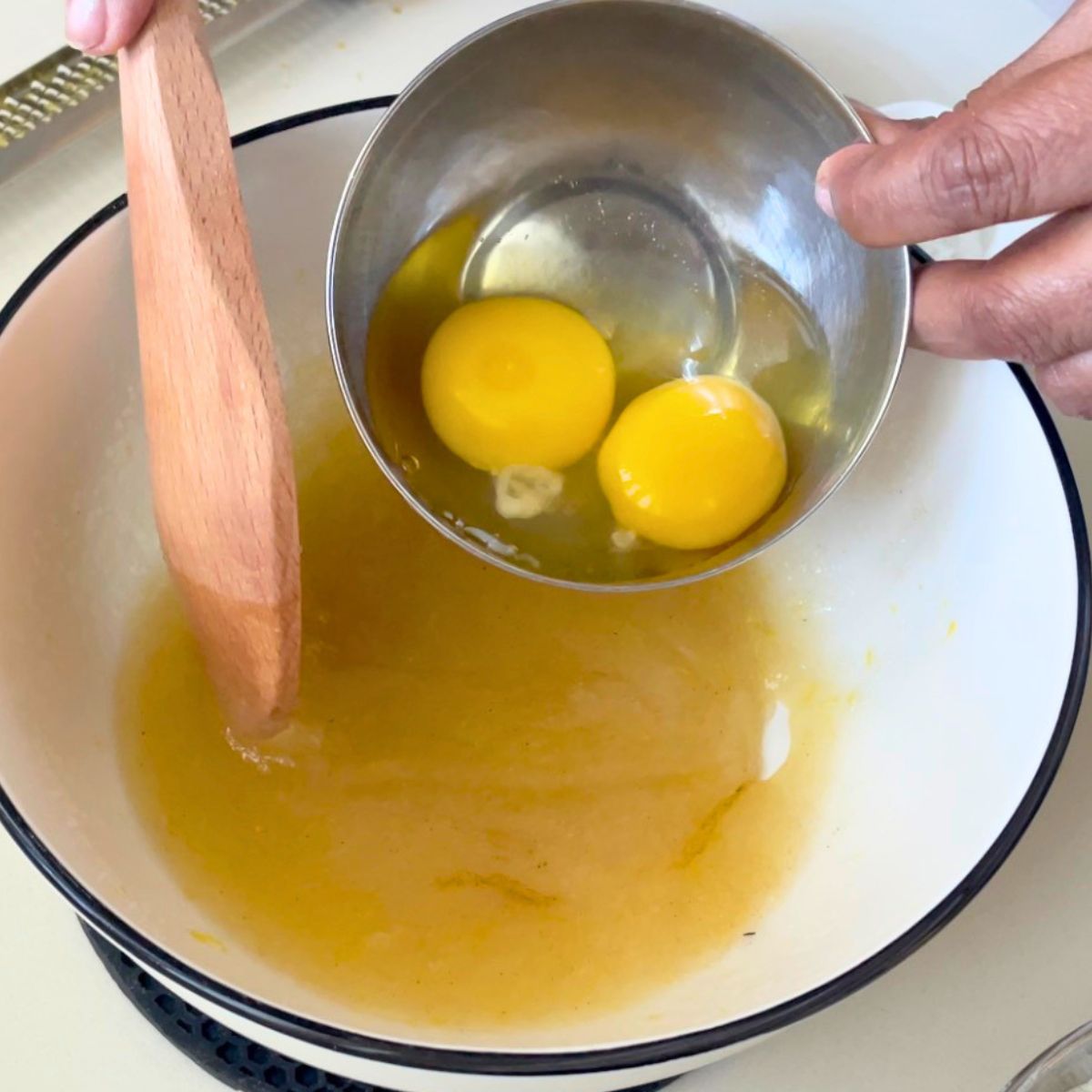 Adding egg and egg yolk to the white bowl.