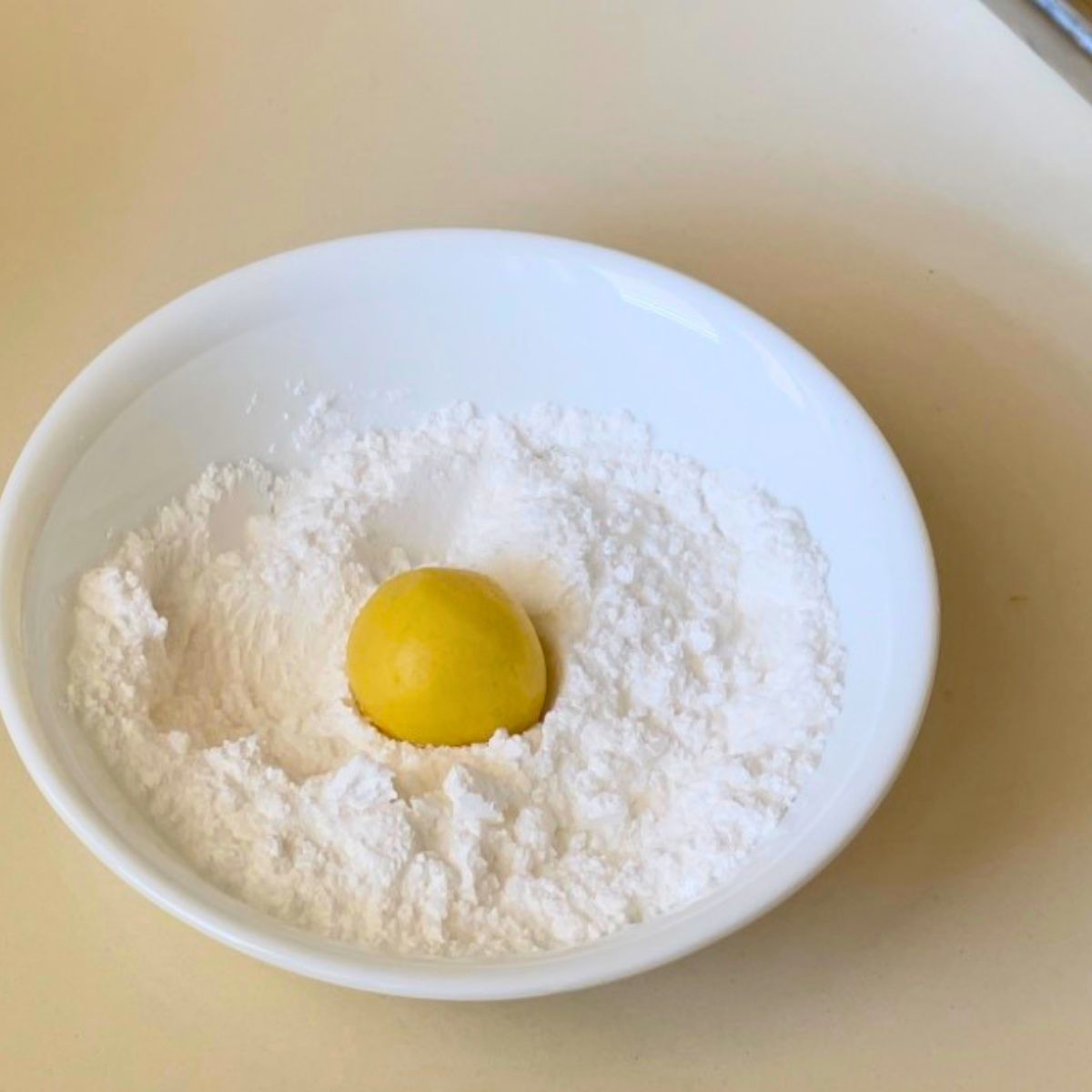 A white bowl dipping crinkle cookies in sugar.