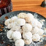 A black plate with snowball cookies.