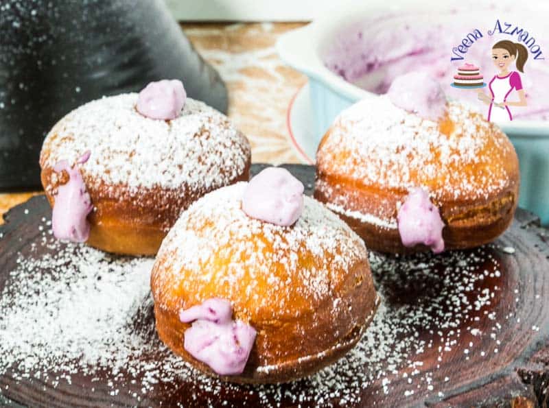 Three raspberry cream doughnuts on a wooden stand.