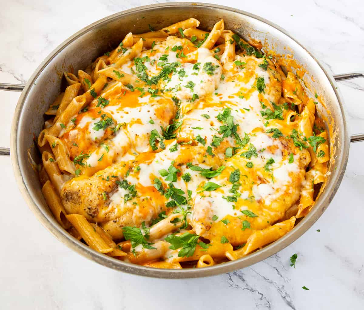 A skillet with cheese topped pasta and chicken.
