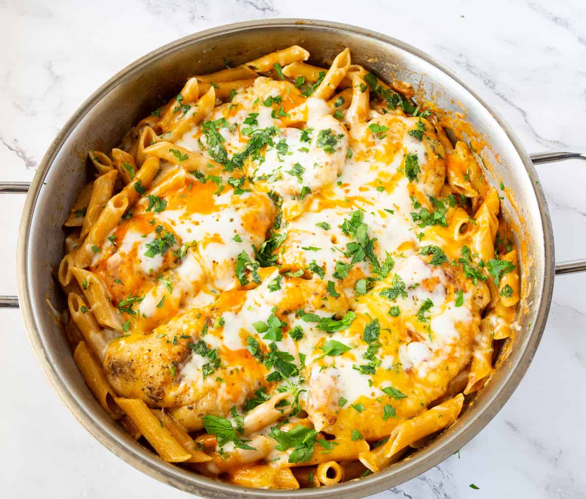 A skillet with pasta topped with chicken breast and cheese. 