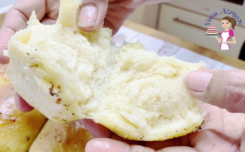 A person breaking in two a garlic dinner roll.