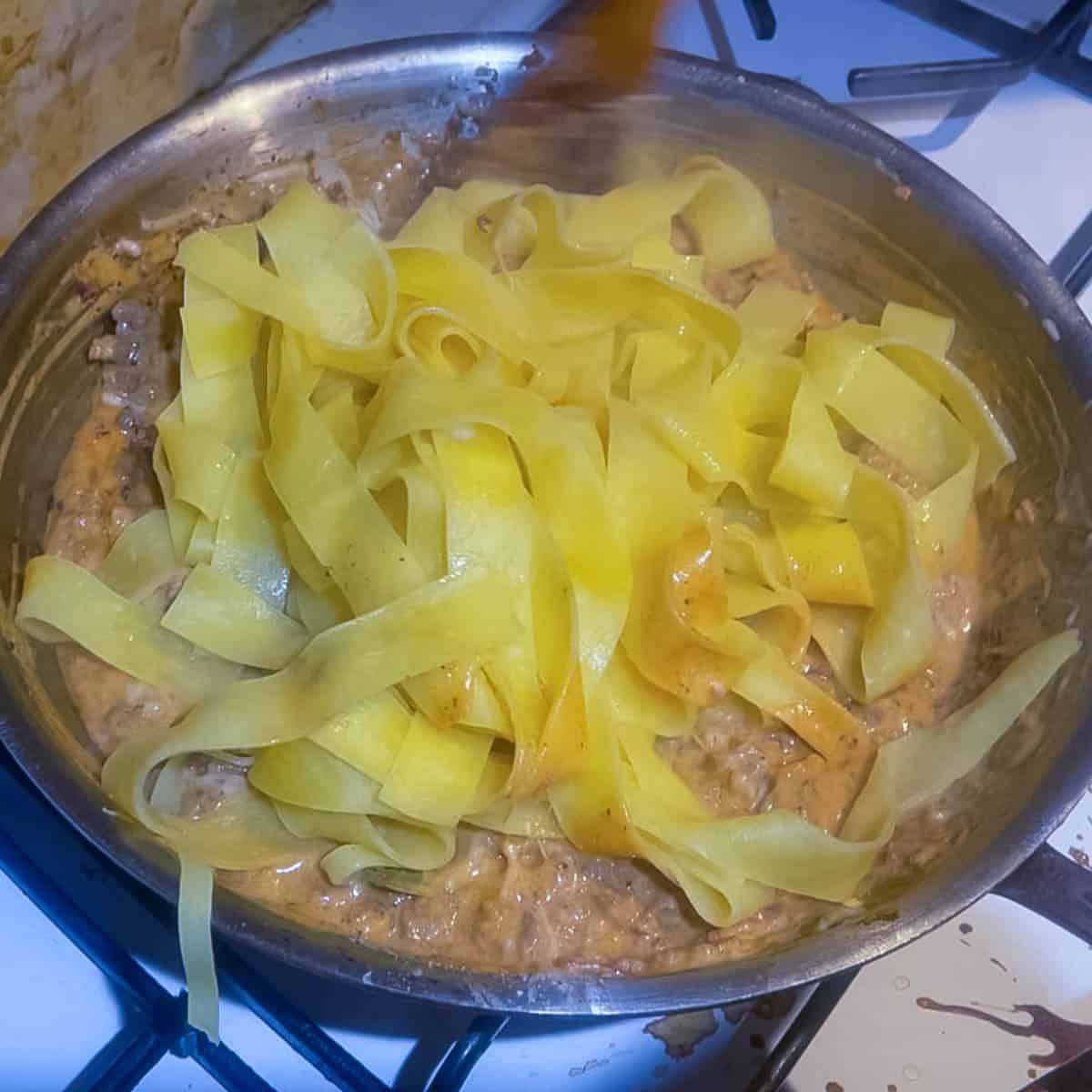 Adding pasta to the ground beef sauce.