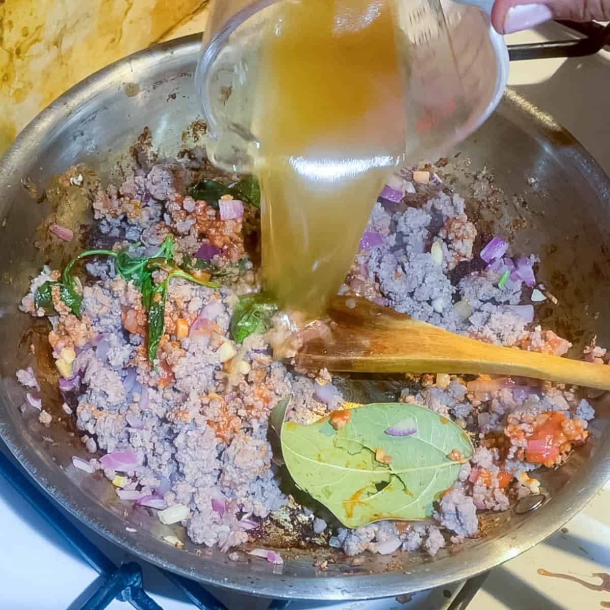 Adding broth to the ground beef sauce.