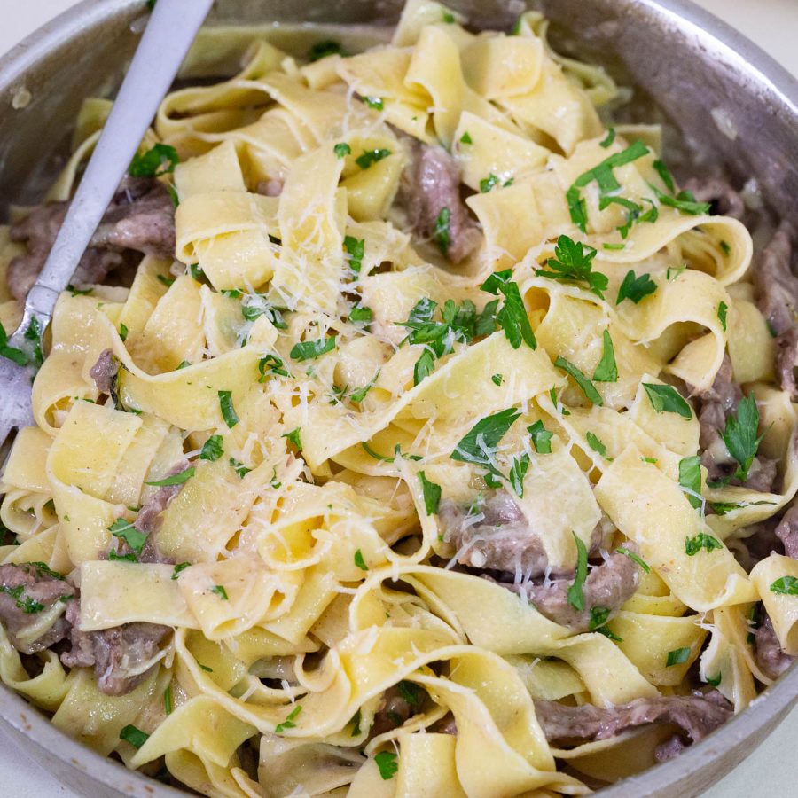 A saute pan with lamb and pasta.