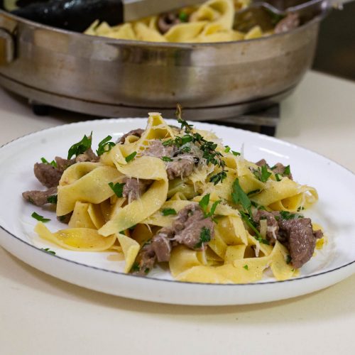 A white plate with lamb pasta.