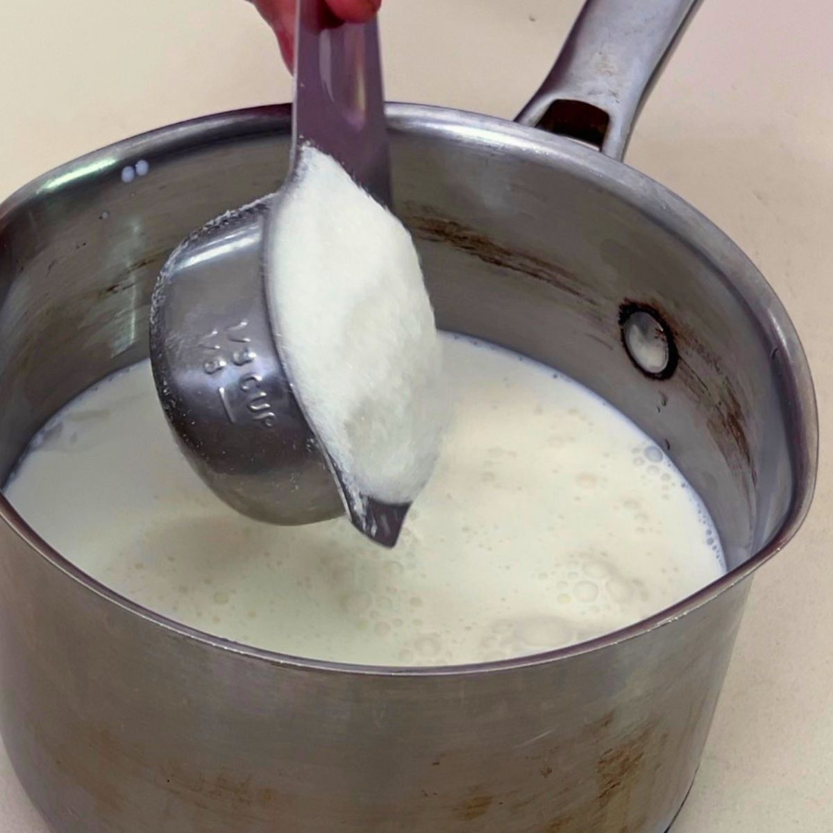 Adding sugar to the milk and cream in saucepan.