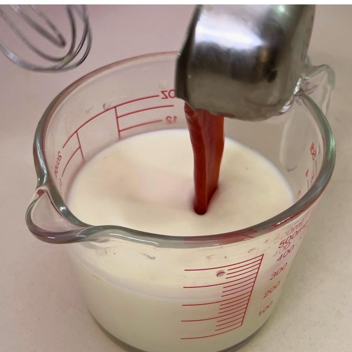 A measuring cup with panna cotta and strawberry sauce.