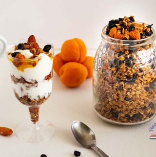 A jar with homemade granola and blueberries next to a glass with yogurt and granola parfait.