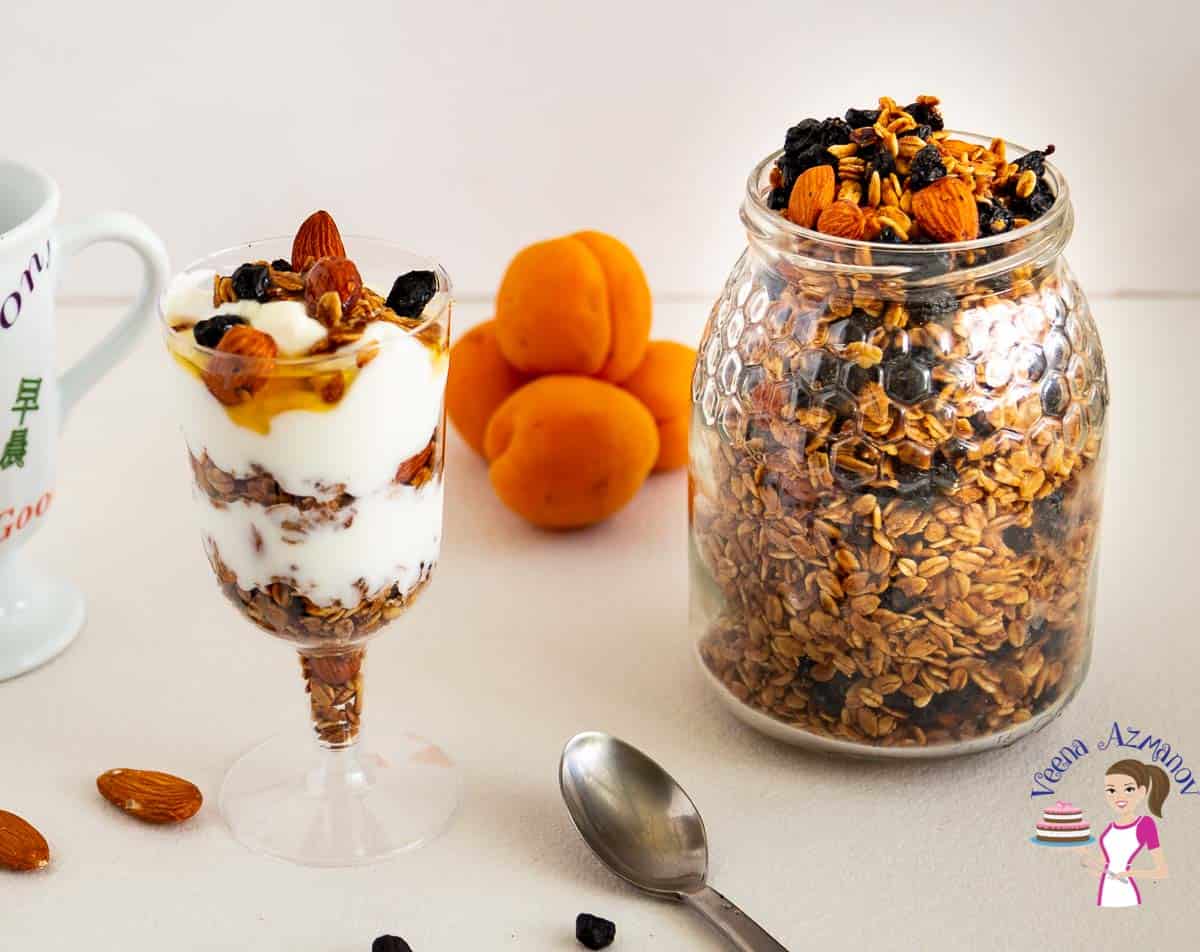 A jar with homemade granola and blueberries next to a glass with yogurt and granola parfait.