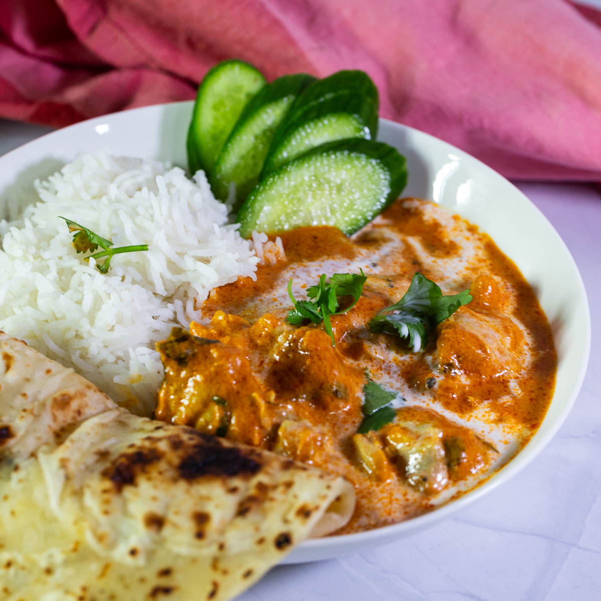 A white plate with Indian butter chicken and rice.