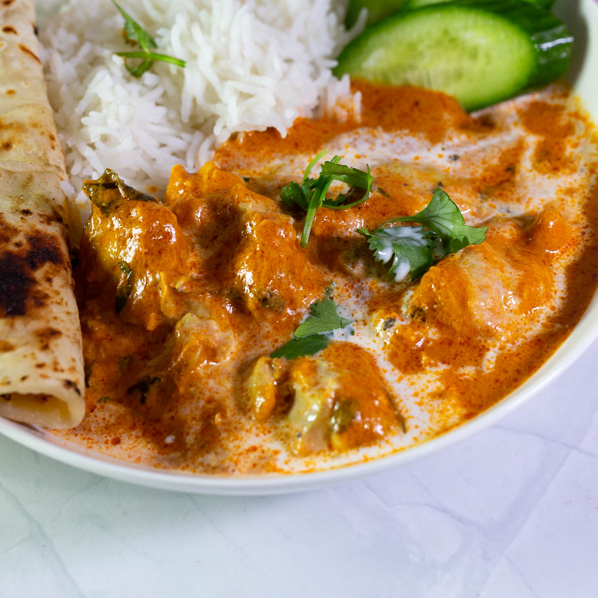 A white plate with rice and butter chicken.