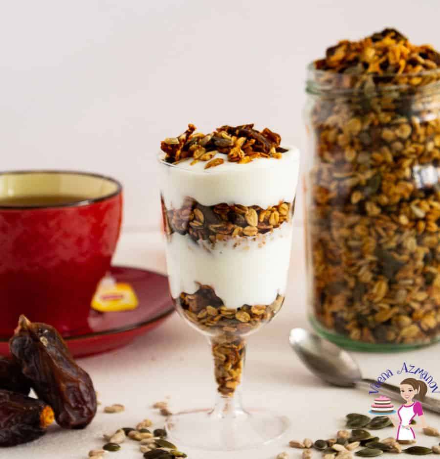 Granola in a jar next to a glass with yogurt parfait, and a cup of tea.