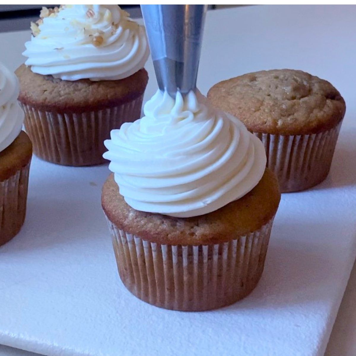 Frosting a banana cupcake with cream cheese swirl.