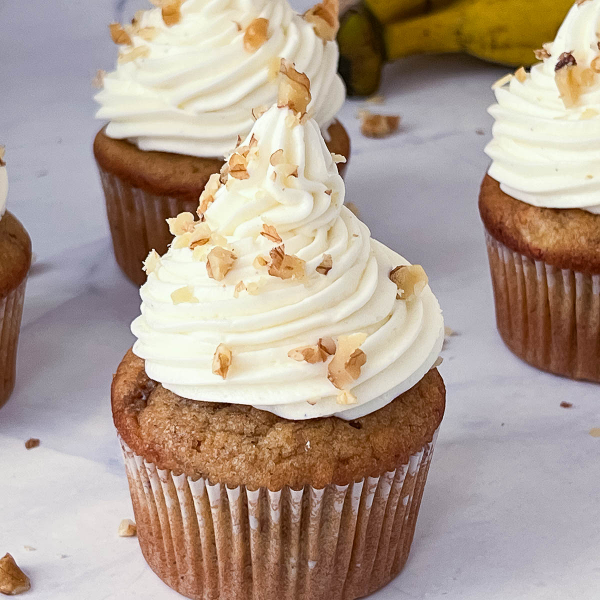 Frosted banana cupcakes with walnuts and cream cheese on the table.