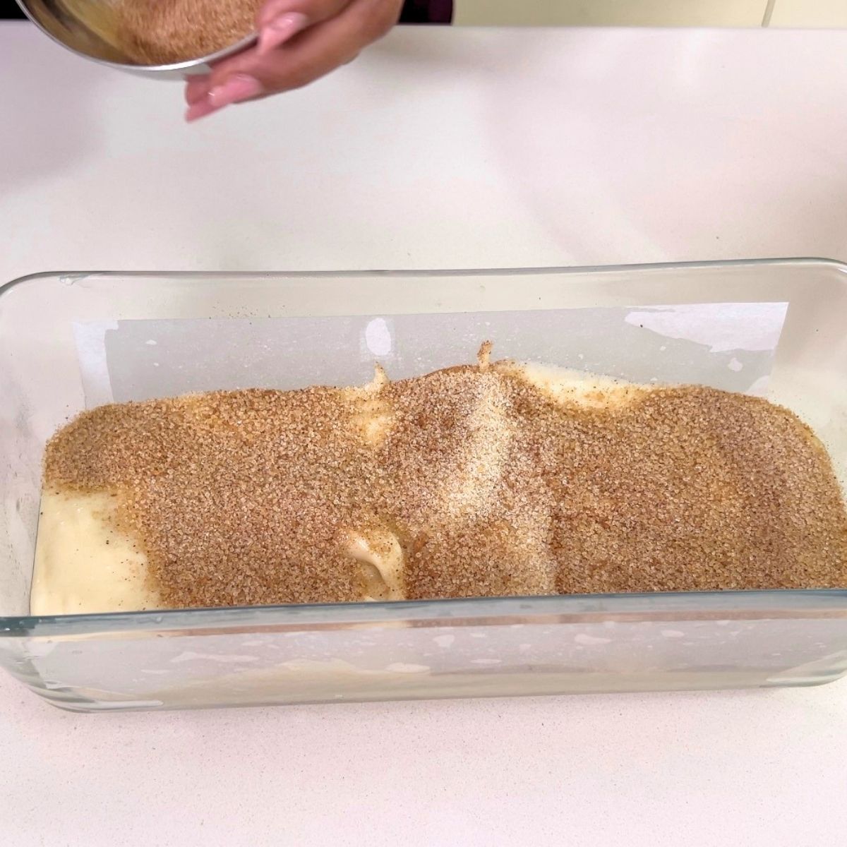 A loaf pan with cake batter and cinnamon sugar.